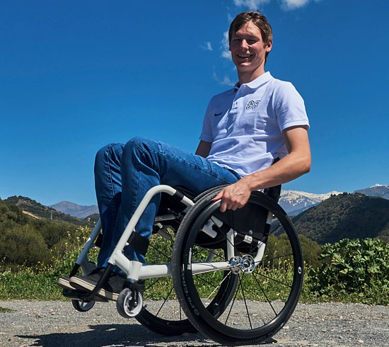 Man sitting on a wheelchair outside, wearing blue jeans and a blue button up 