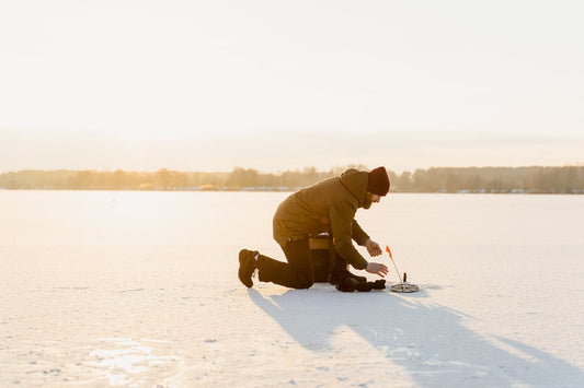 Man in warm clothes kneeling on the snow with a tool
