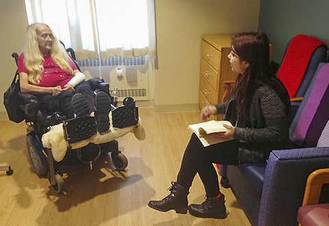 A women with white hair in a wheel chair, and another women sitting taking notes.