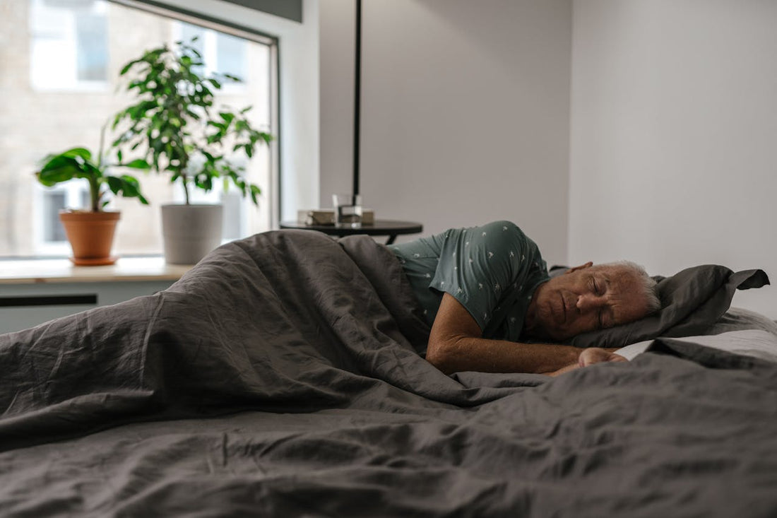 Senior man sleeping on his right side, with a grey blanket
