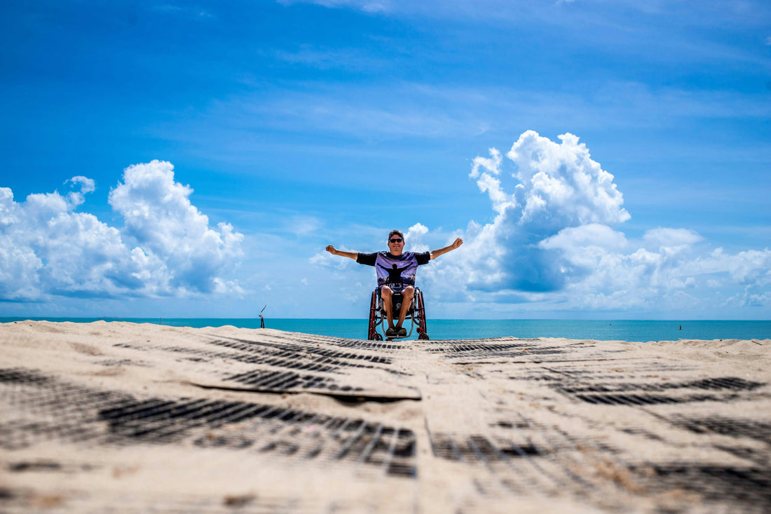 A man at the beach, with a beautiful blue sky and in a wheel hair with their arms up.