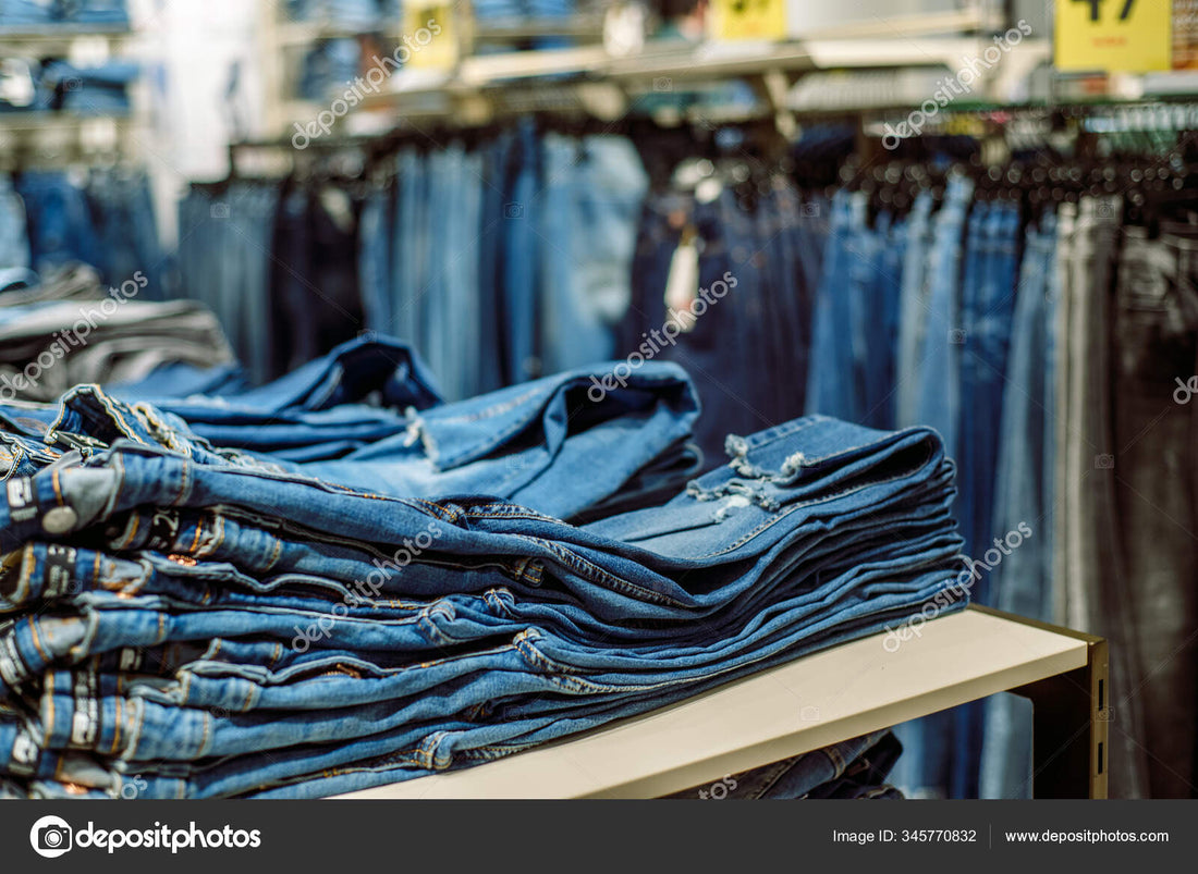 A rack filled with different colour jeans, in front of it is a table folded with blue jeans
