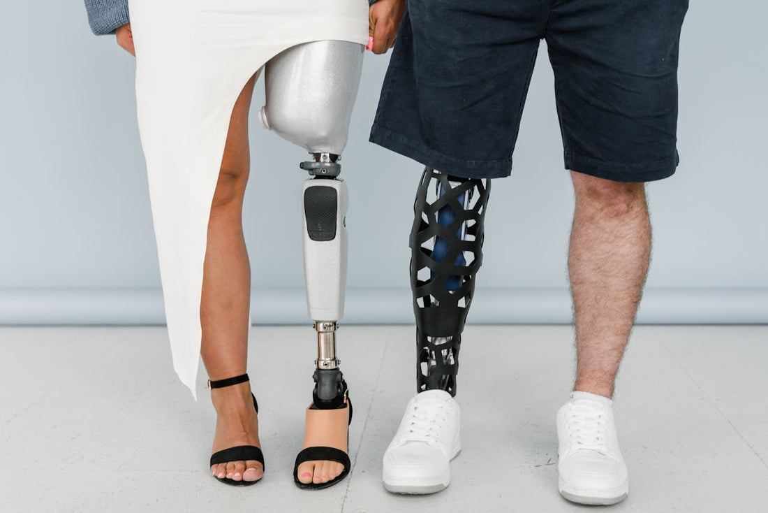 Close-up of two people standing side by side, each with a prosthetic leg. One person is wearing a white skirt and black sandals, while the other is in black shorts and white sneakers