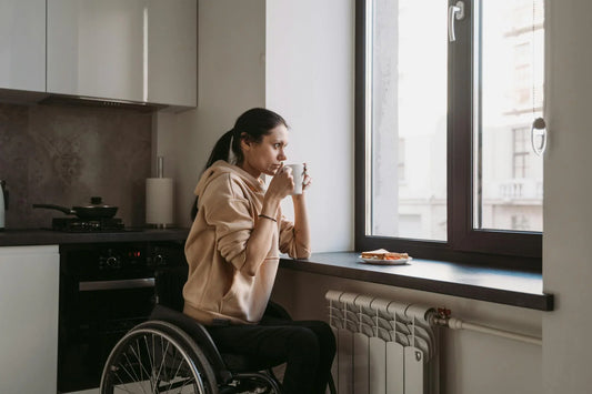 women in wheelchair drinking coffee looking out window 