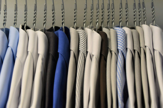 A row of neatly hung dress shirts on twisted metal hangers, featuring a range of colors and patterns including white, blue, gray, and checkered designs