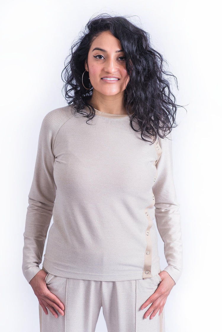 Woman smiling wearing cream long sleeve crewneck top with side snap closures.