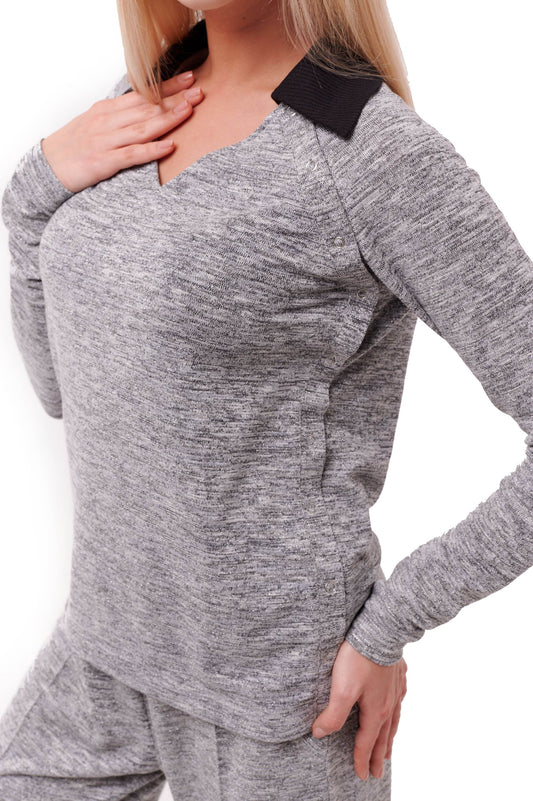 Woman wearing grey long sleeve top with black collar and side snap closures.