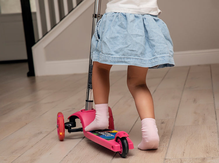 Child riding on scooter wearing light pink anti slip socks with tread pattern.