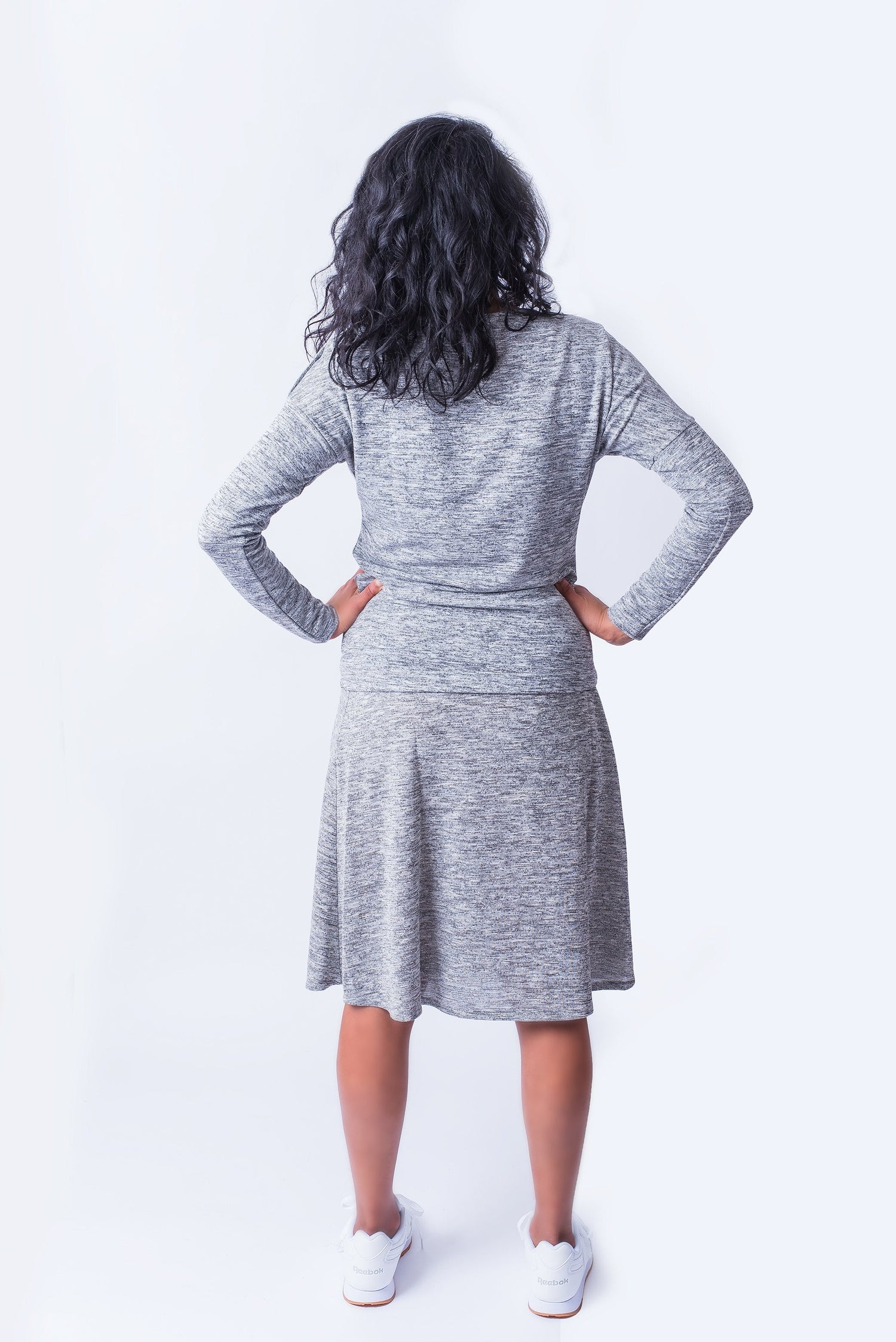 Woman facing backwards wearing grey long sleeve top and matching grey skirt.