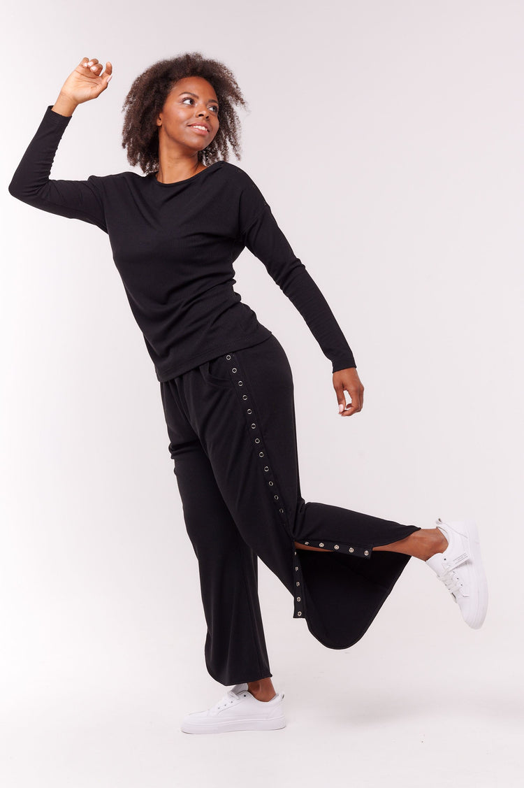 Woman posing wearing black long sleeve top with shoulder snap closures and matching pants.