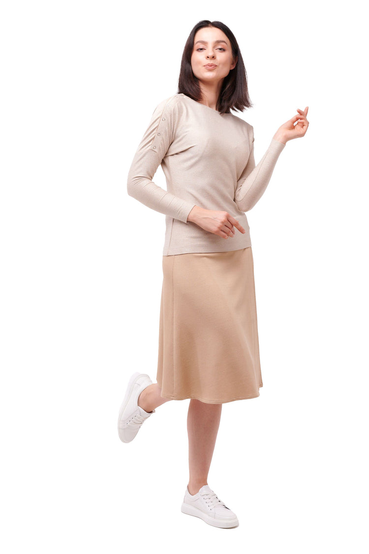 Woman posing wearing cream long sleeve top  with shoulder snap closures and light brown skirt.