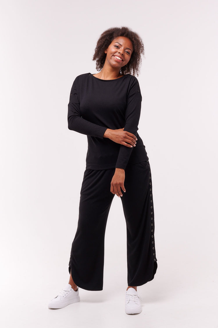 Woman posing wearing black long sleeve top with shoulder snap closures and matching pants.