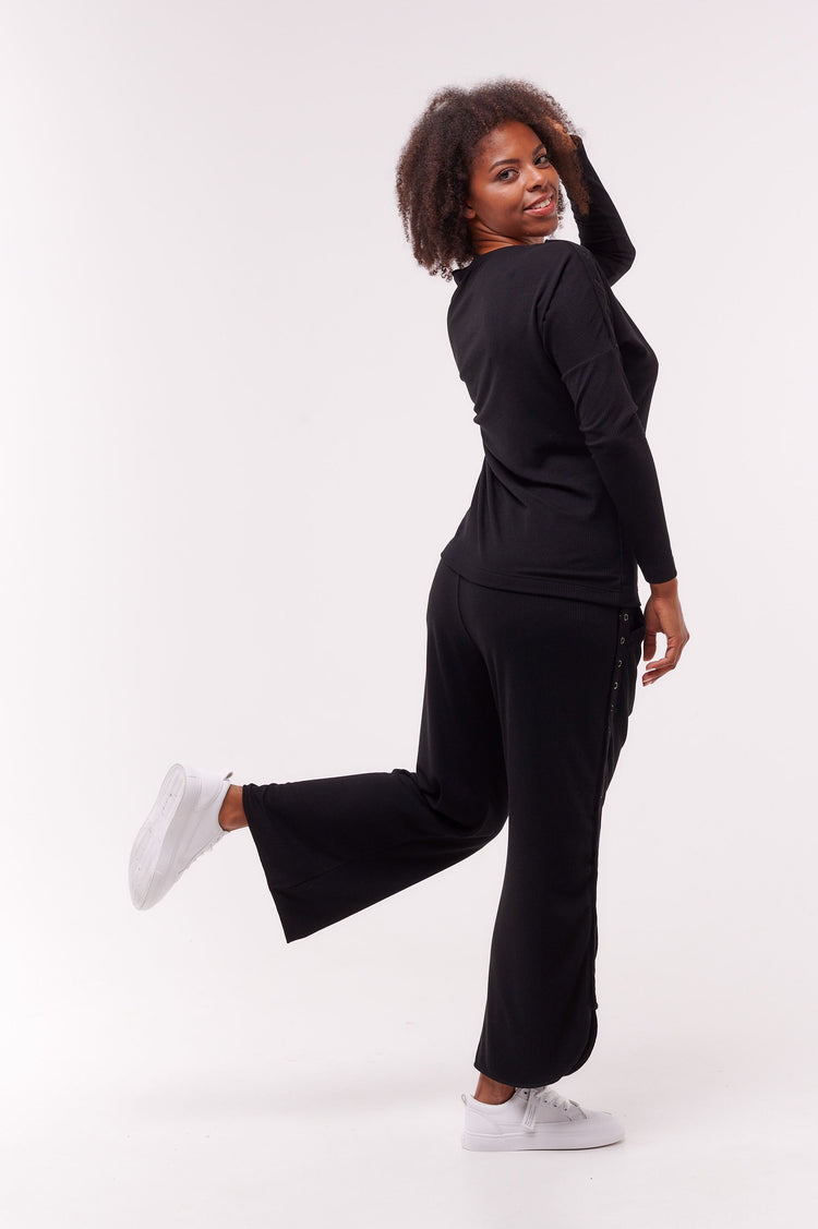 Woman posing wearing black long sleeve top with shoulder snap closures and matching bottoms.