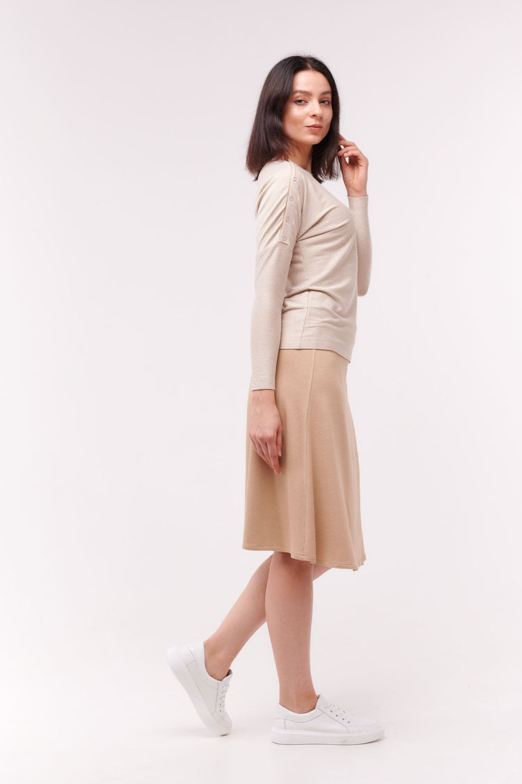 Woman posing wearing cream long sleeve top with shoulder snap closures and light brown skirt.