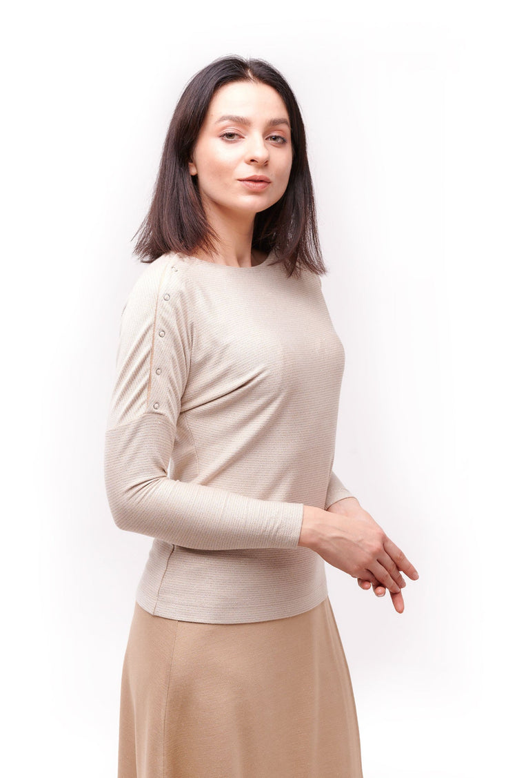 Woman posing wearing cream long sleeve top  with shoulder snap closures and light brown skirt.