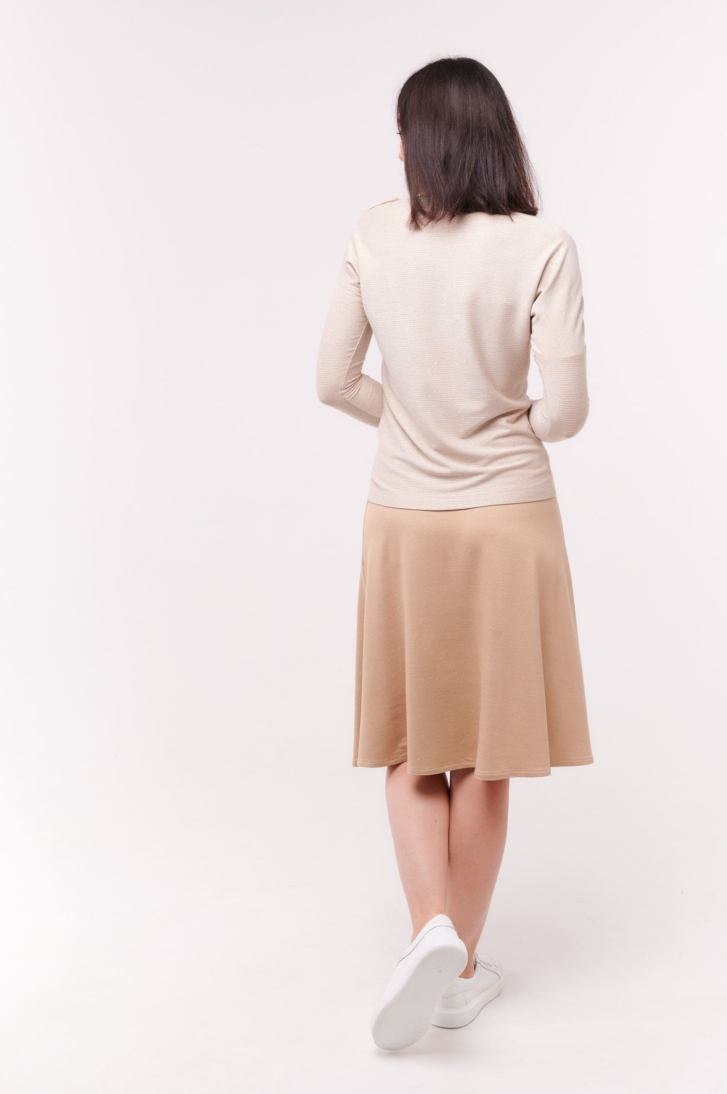 Woman turned away wearing cream long sleeve top with shoulder snap closures and skirt.