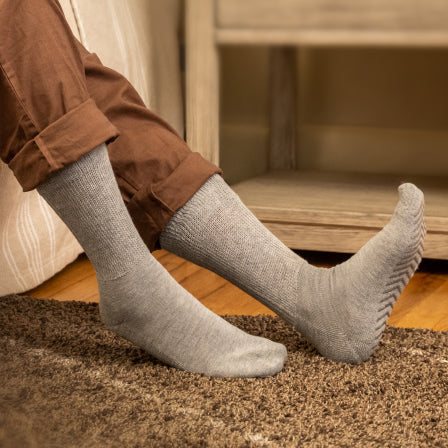Model wearing light grey anti slip diabetic socks with tread pattern on the bottom.