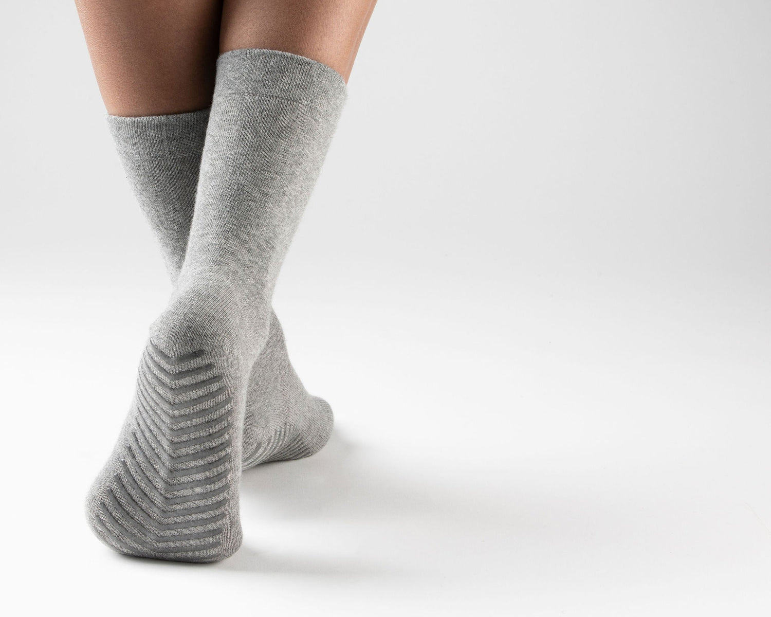 Model wearing light grey anti slip socks with tread pattern on the bottom.