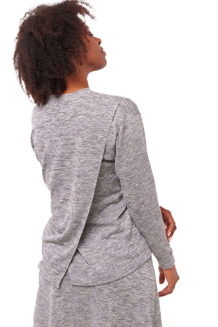 Woman wearing grey long sleeve top with back overlap and shoulder snap closures.