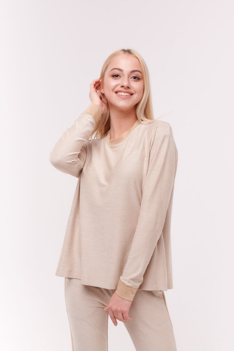 Woman smiling wearing cream long sleeve top with back overlap and shoulder snap closures.