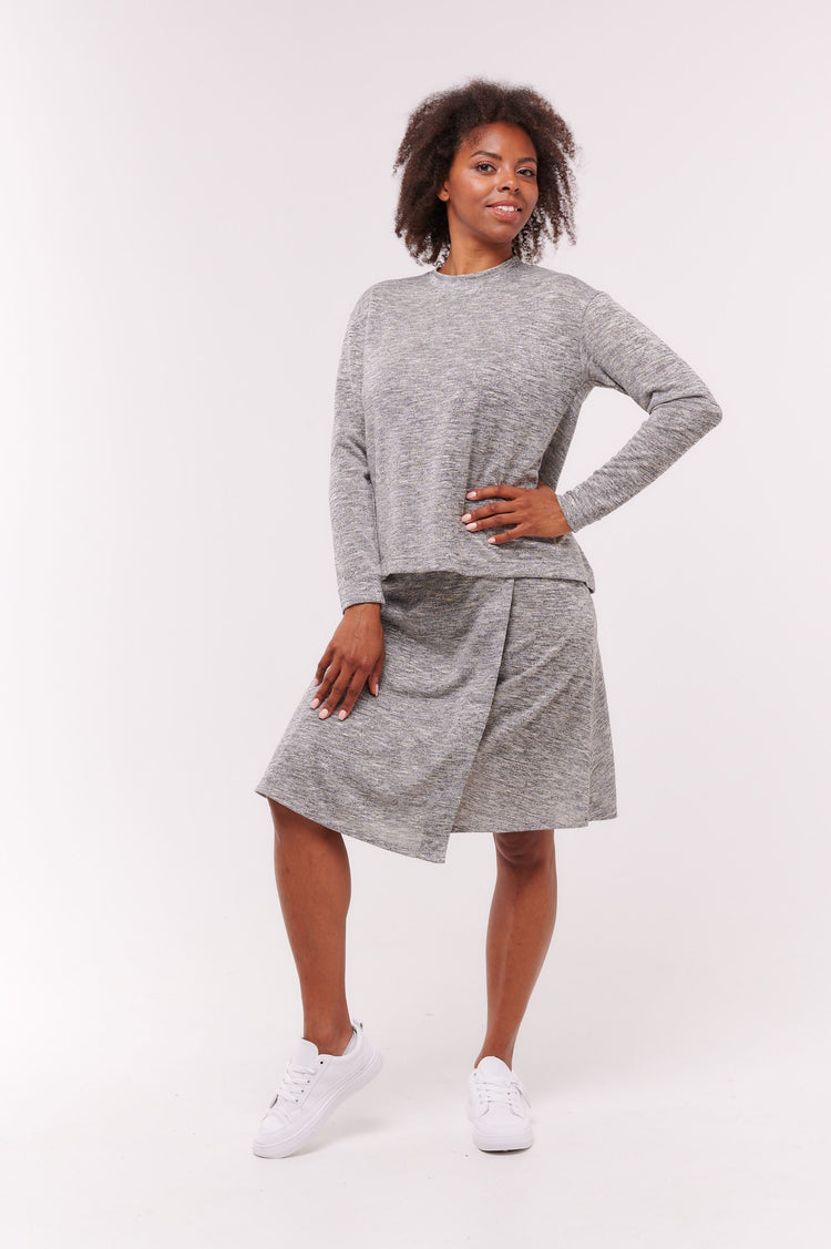 Woman posing wearing grey long sleeve top with back overlap and grey skirt.