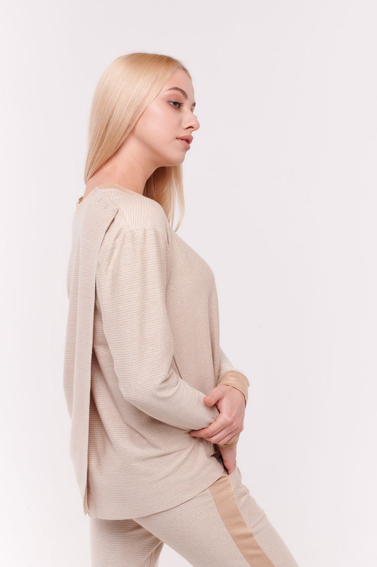 Woman posing wearing cream long sleeve top with back overlap and shoulder snap closures.