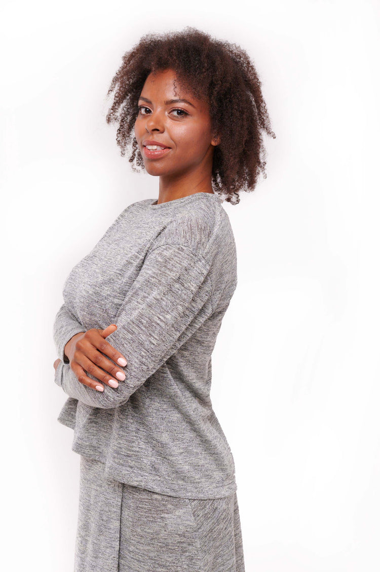 Woman wearing grey long sleeve top with back overlap and shoulder snap closures.