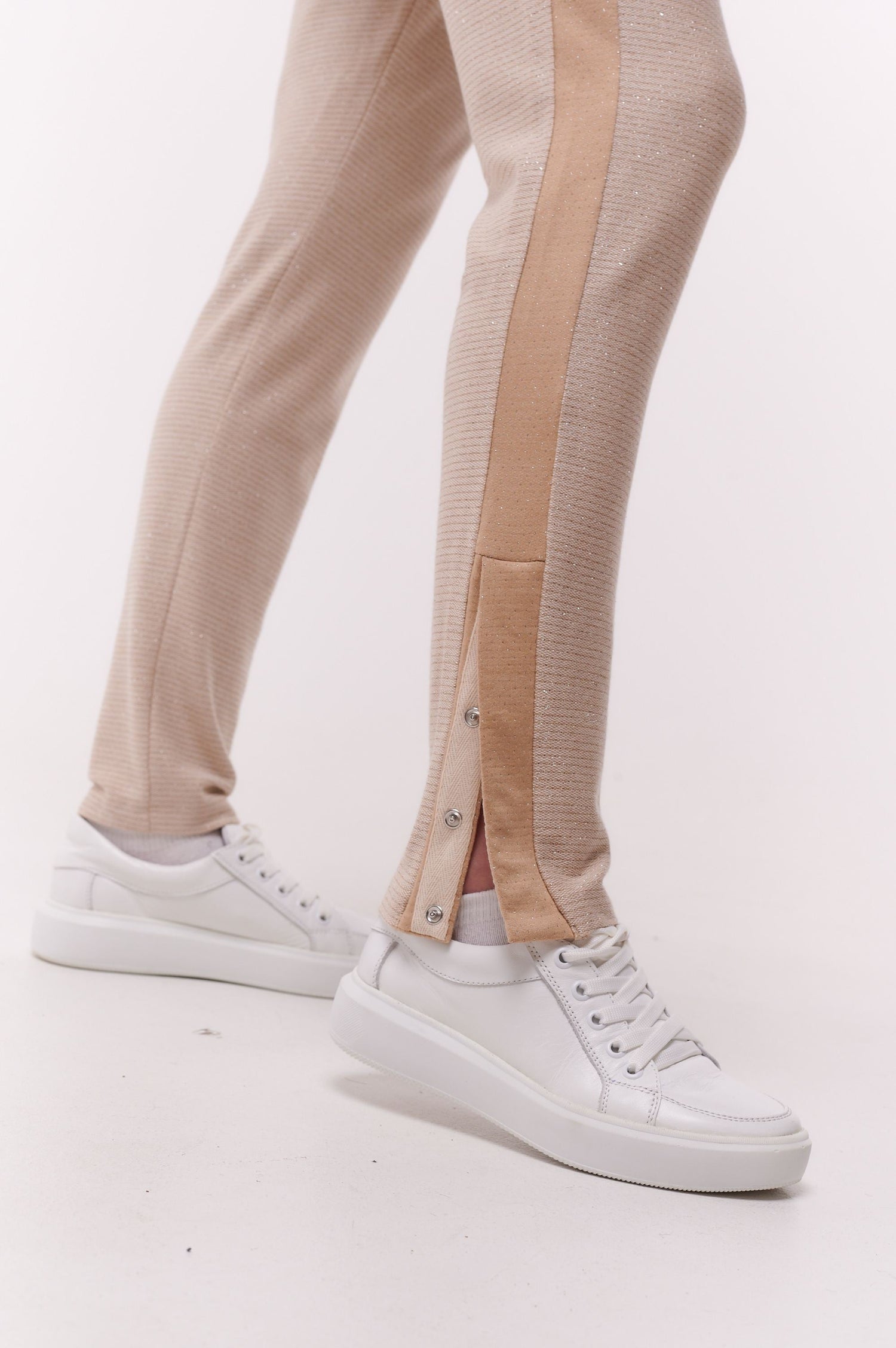Close up of woman wearing cream full length slim pants with ankle snap closures.
