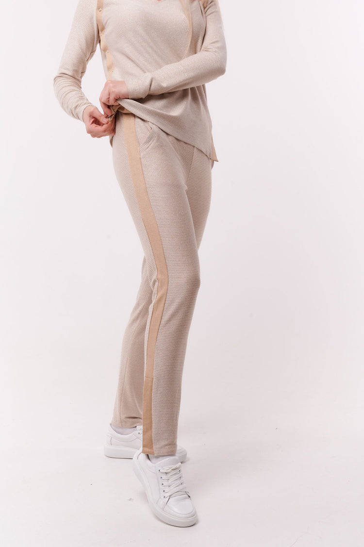 Woman wearing cream full length slim pants with ankle snap closures and matching top.