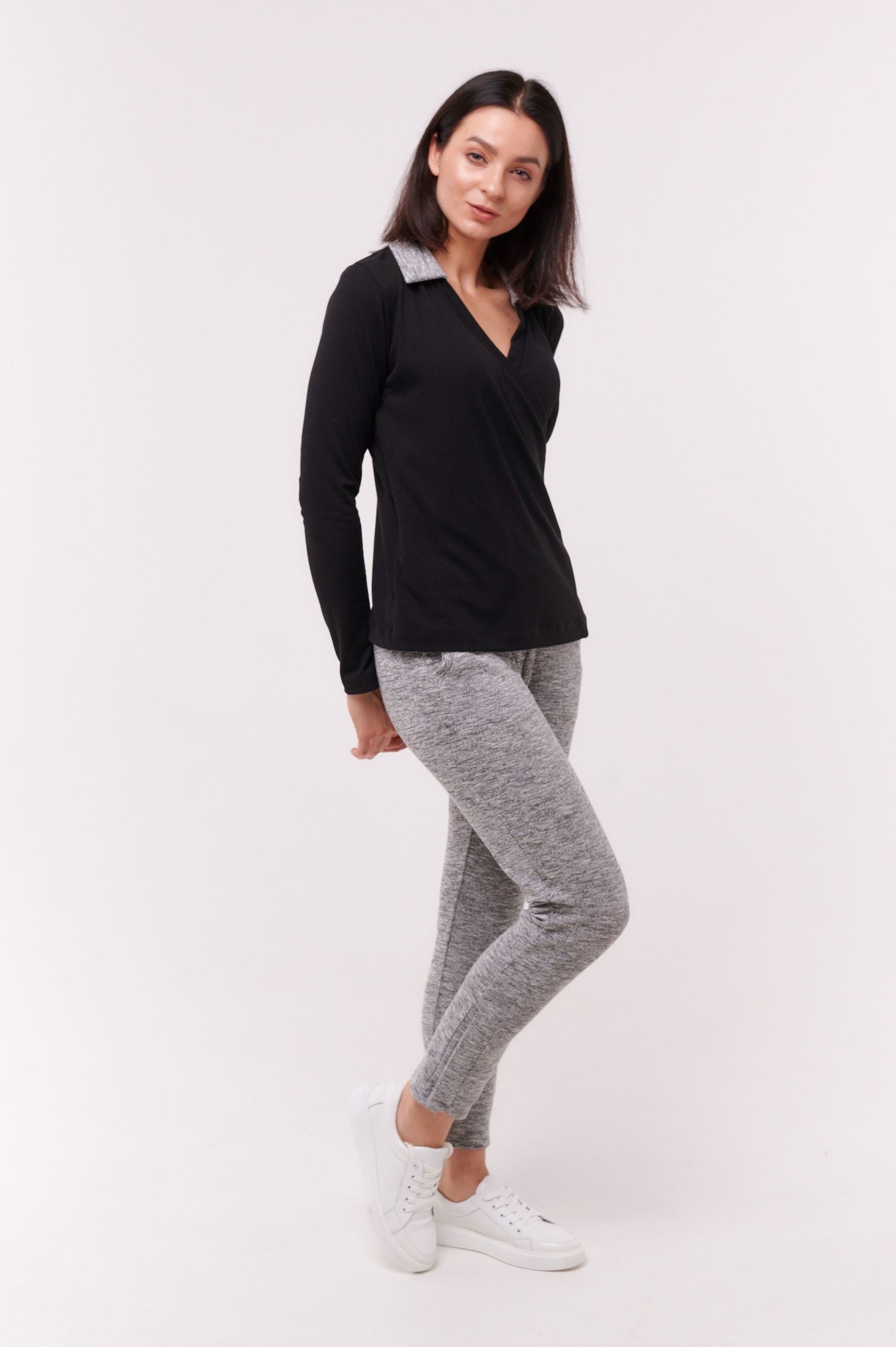 Woman wearing black long sleeve wrap top with side snap closures and grey pants.