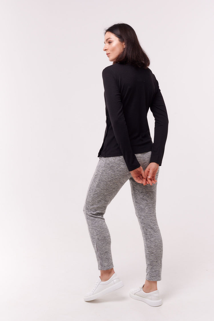 Woman wearing black long sleeve wrap top with side snap closures and grey pants.