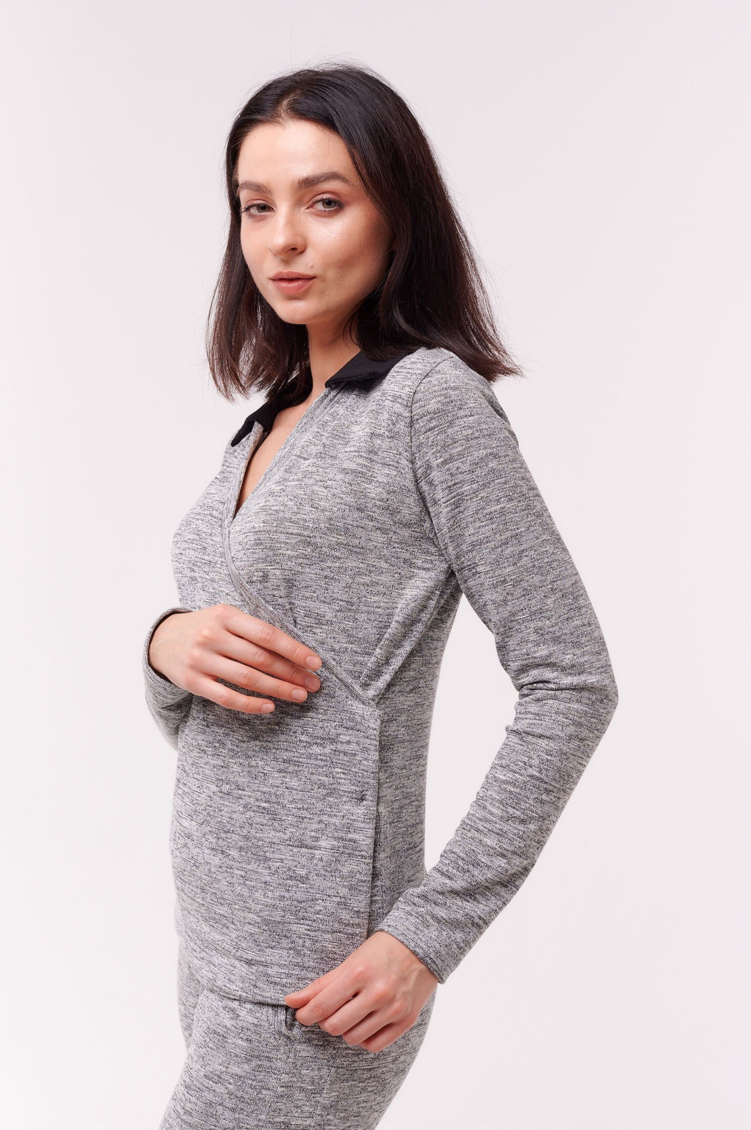 Woman wearing grey long sleeve wrap top with black collar and side snap closures.